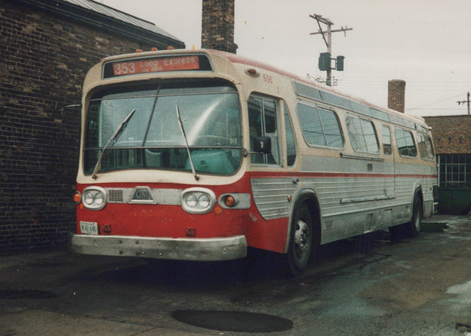 A red and cream CTA New Look bus, number 606, parked on a wet street with a brick building behind it, displaying route 353 Loop Express on its destination sign.