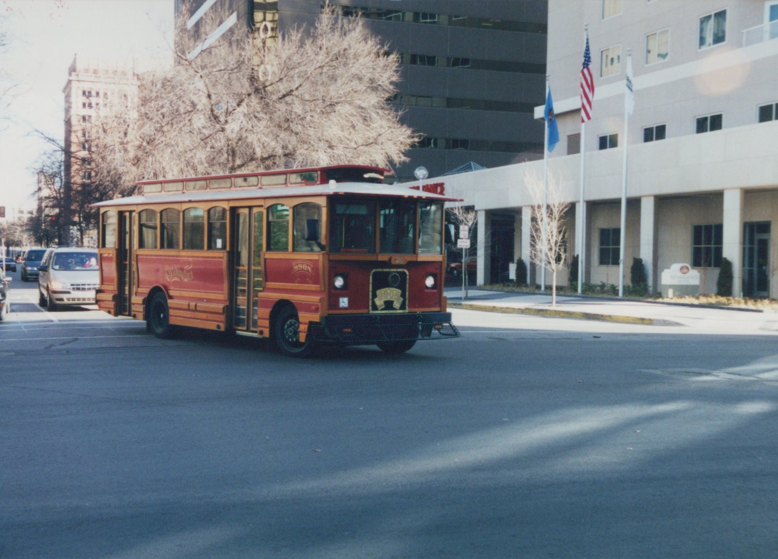 A red and wood-paneled trolleybus number 9908 with 'Oklahoma Spirit' lettering is parked on a city street in front of a Renaissance Hotel, with bare trees and a clear sky.