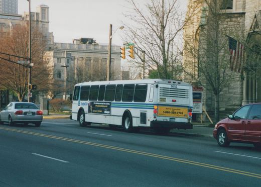A white IndyGo bus with fleet number 8652, carrying a 'Census 2000' ad, travels down a city street lined with trees and buildings.