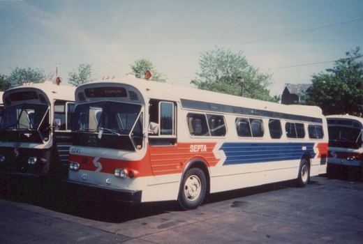 A white, red, and blue SEPTA bus, number 6241, is parked in a lot on a sunny day with other buses nearby.