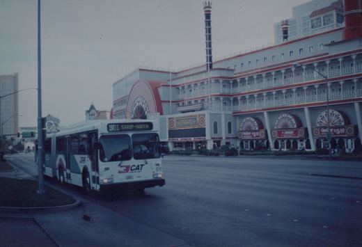 A white, teal, and magenta Clark County Area Transit bus with the number 515 and route 301 to Strip-South is shown on a city street, with a large, ornate building in the background.