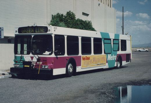 A side view of a Metro bus with the number 4037 and 'Green Line' on the front sign, parked on an asphalt lot with a white building and a pickup truck in the background.