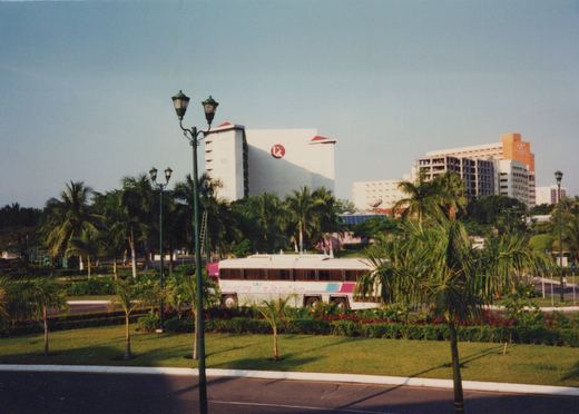 A white bus with 'Principe Ejecutivo' lettering on its side is parked near palm trees and manicured lawns, with large resort hotels in the background under a clear blue sky.