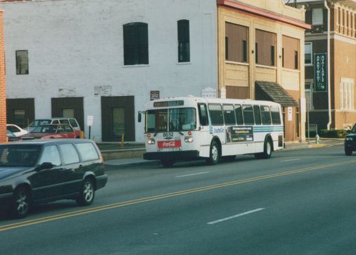 A white IndyGo motor bus, number 8652, is driving on a city street with a Coca-Cola logo on its front and other cars nearby.