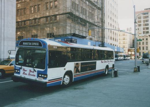 A white, blue, and red New York Bus Service motor bus, number 1658, labeled 'Manhattan Express,' is parked on a city street with scaffolding-covered buildings in the background.