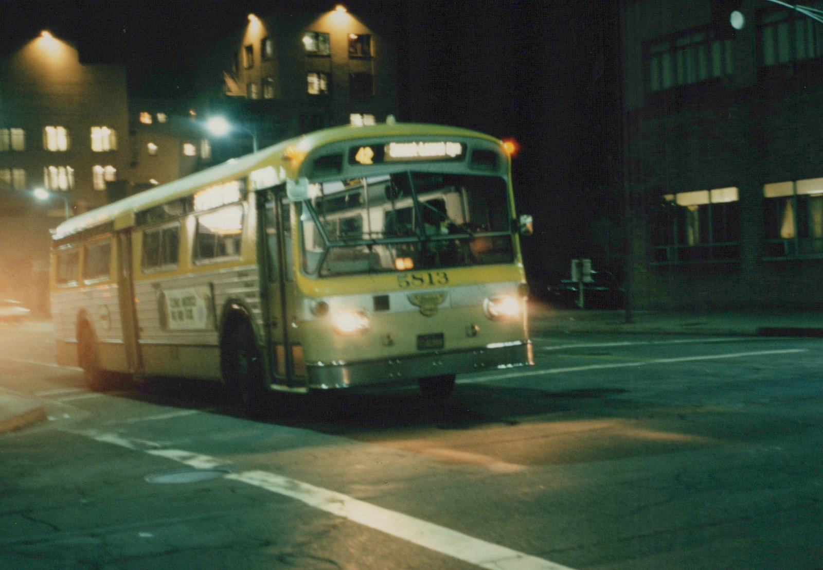 A yellow and white CTA bus numbered 5813 drives down a city street at night, its headlights on and its destination sign reading 42 South-Central Exp.