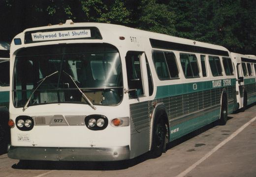 A white and green Transit Systems motor bus with the number 977 and a destination sign reading 'Hollywood Bowl Shuttle' is parked in a lot.