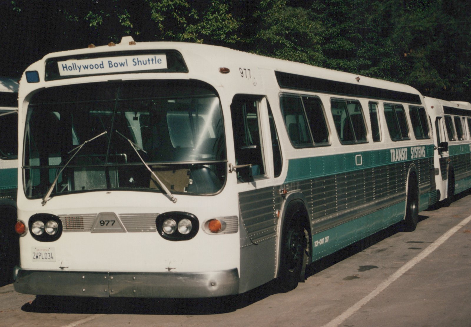 A white and green Transit Systems motor bus with the number 977 and a destination sign reading 'Hollywood Bowl Shuttle' is parked in a lot.