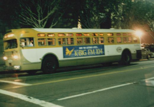 A yellow and white CTA bus with the number 30759 on its rear is driving down a city street at night; a blue and yellow 'K-BIG FM 104' ad is visible on its side.