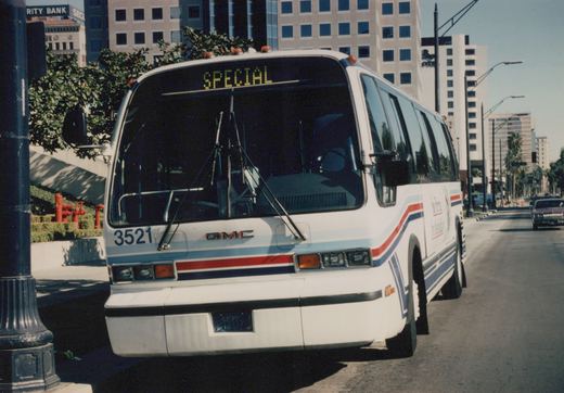 Front three-quarter view of a white Southern Pacific GMC RTS bus with red and blue stripes, fleet number 3521, parked on a city street under a clear sky.