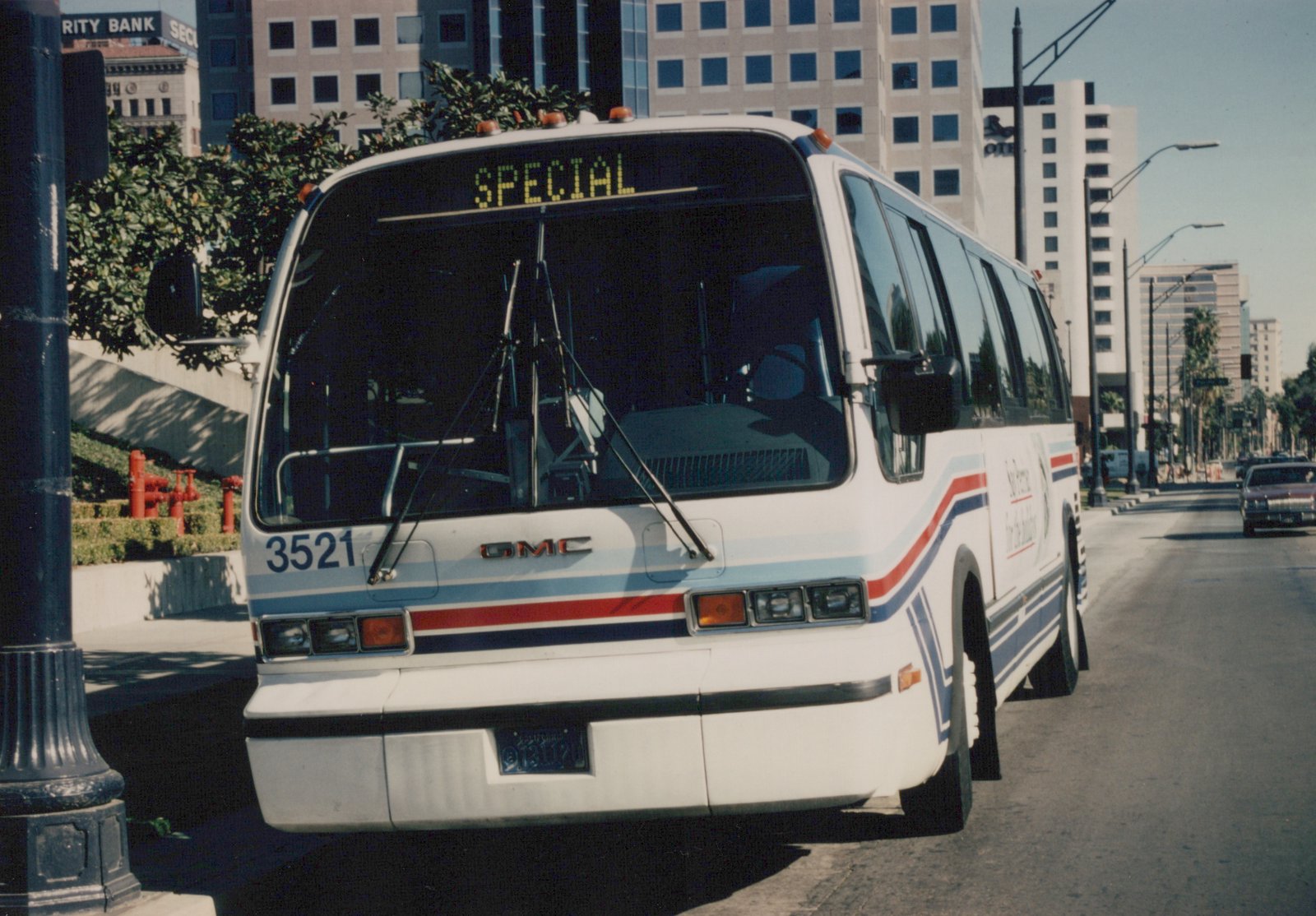 Front three-quarter view of a white Southern Pacific GMC RTS bus with red and blue stripes, fleet number 3521, parked on a city street under a clear sky.