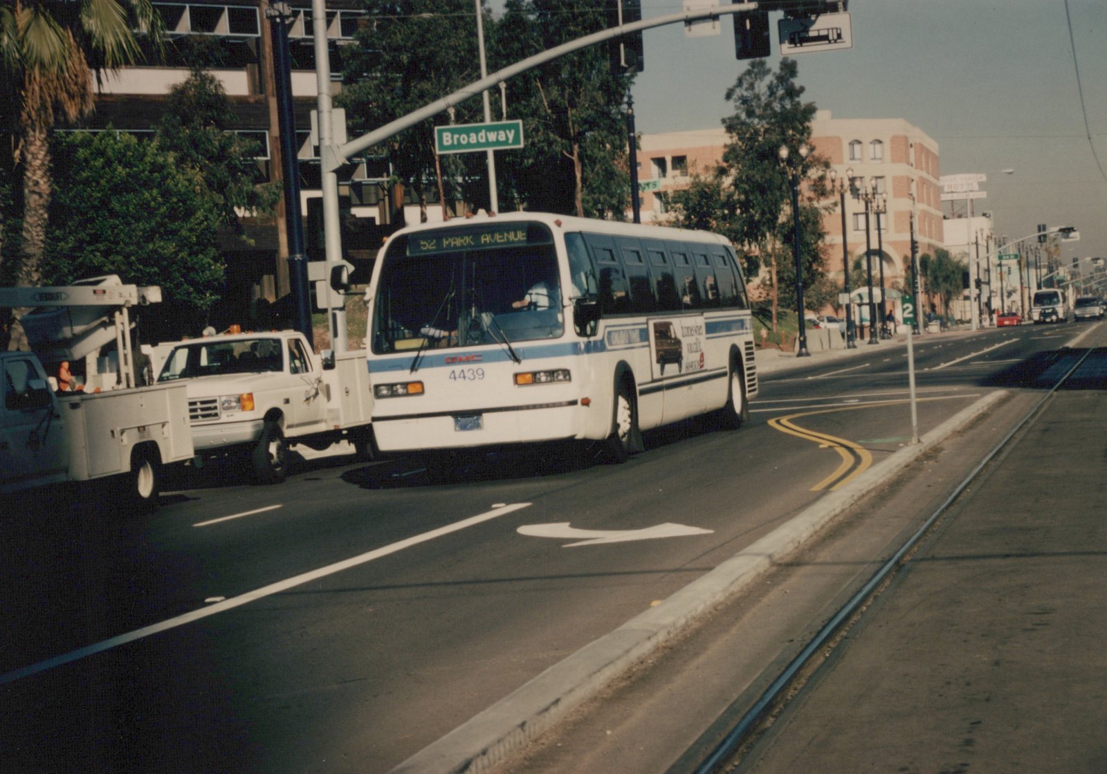 A white and blue Chicago Transit Authority bus, number 4439, on route 52 Park Avenue, is shown driving on a city street with a street sign for Broadway and abandoned streetcar tracks in the road.