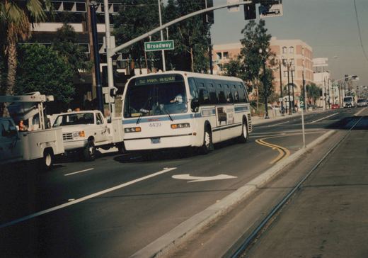 A white and blue Chicago Transit Authority bus, number 4439, on route 52 Park Avenue, is shown driving on a city street with a street sign for Broadway and abandoned streetcar tracks in the road.