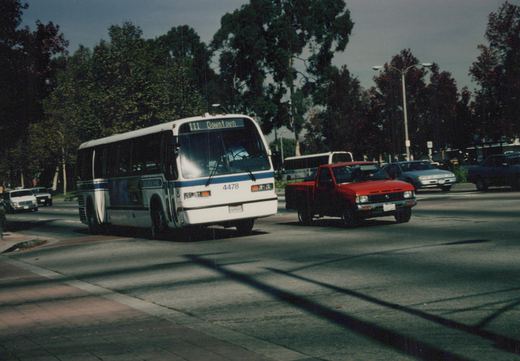 A white and blue bus with the number 4478 and destination sign reading '111 Downtown' is driving on a street with other vehicles, including a red pickup truck, under an overcast sky.
