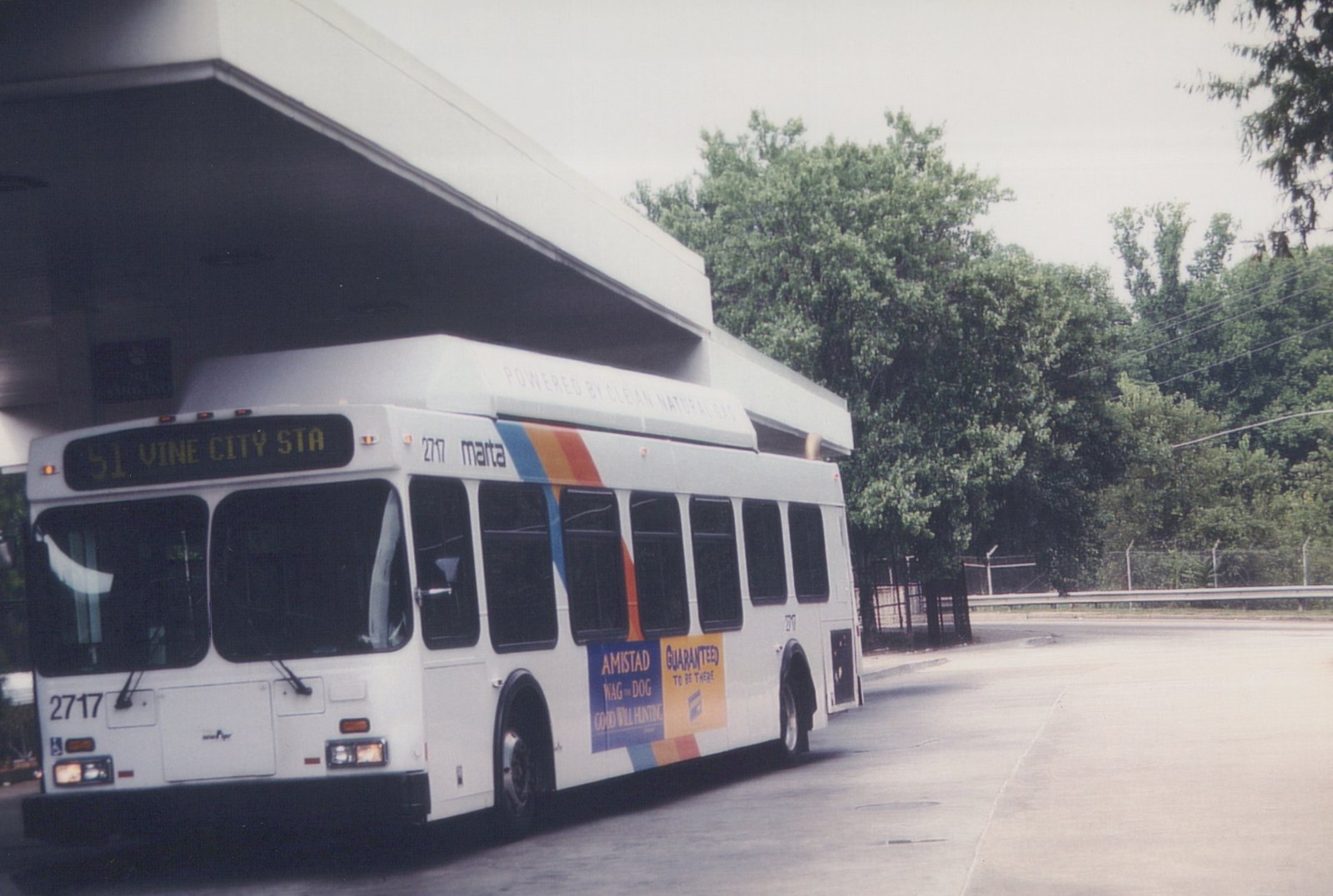 A white MARTA bus with the number 2717 and a destination sign reading '51 VINE CITY STA' is parked at a terminal on a cloudy day, with trees and a fence in the background.