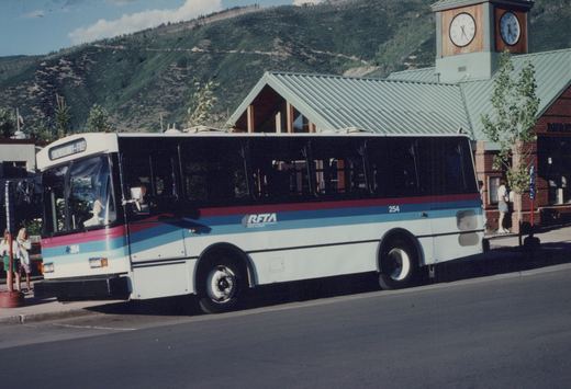 A white, red, and blue RFTA bus, number 254, is parked at a street stop with mountains in the background.