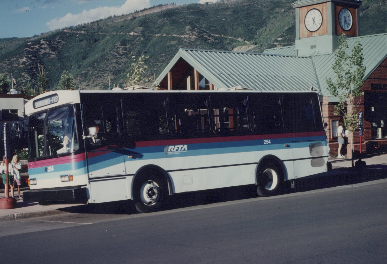 A white, red, and blue RFTA bus, number 254, is parked at a street stop with mountains in the background.
