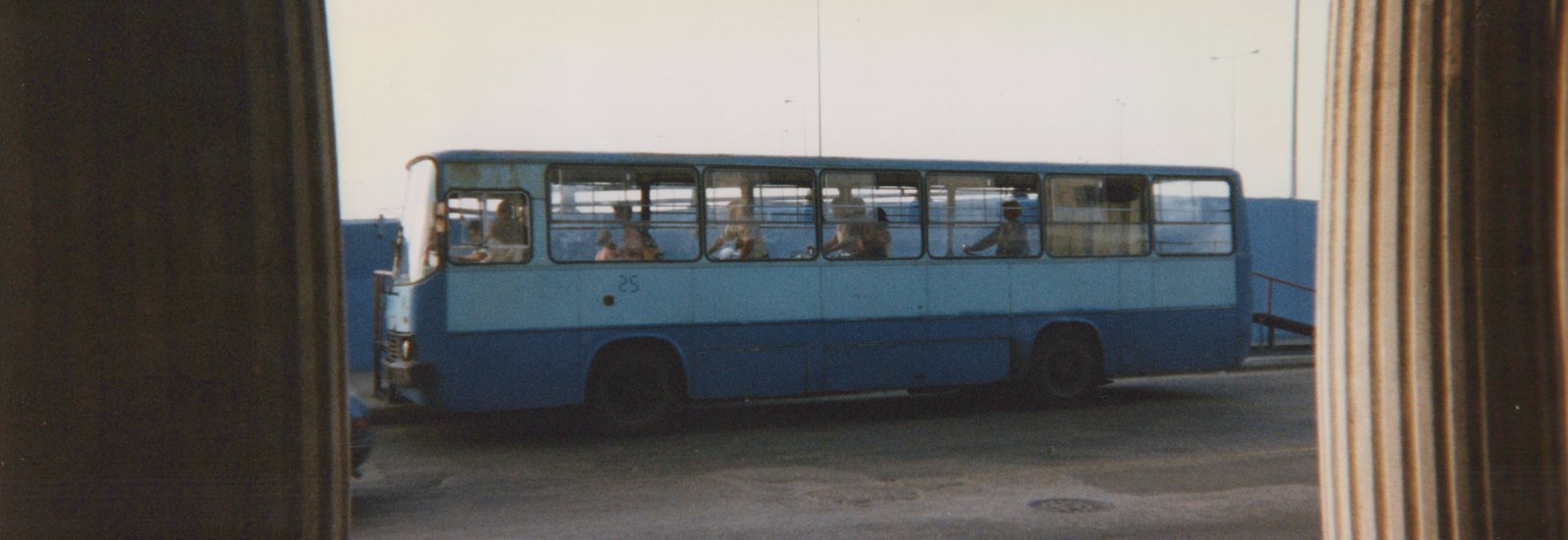 Side view of a blue CTA bus with passengers inside, framed by pillars in the foreground.