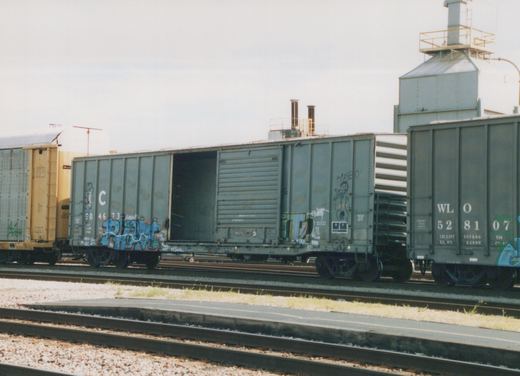 Several boxcars, including Illinois Central 504673 and WL O 528107, are parked on parallel tracks in a gravel yard, with industrial buildings in the background.