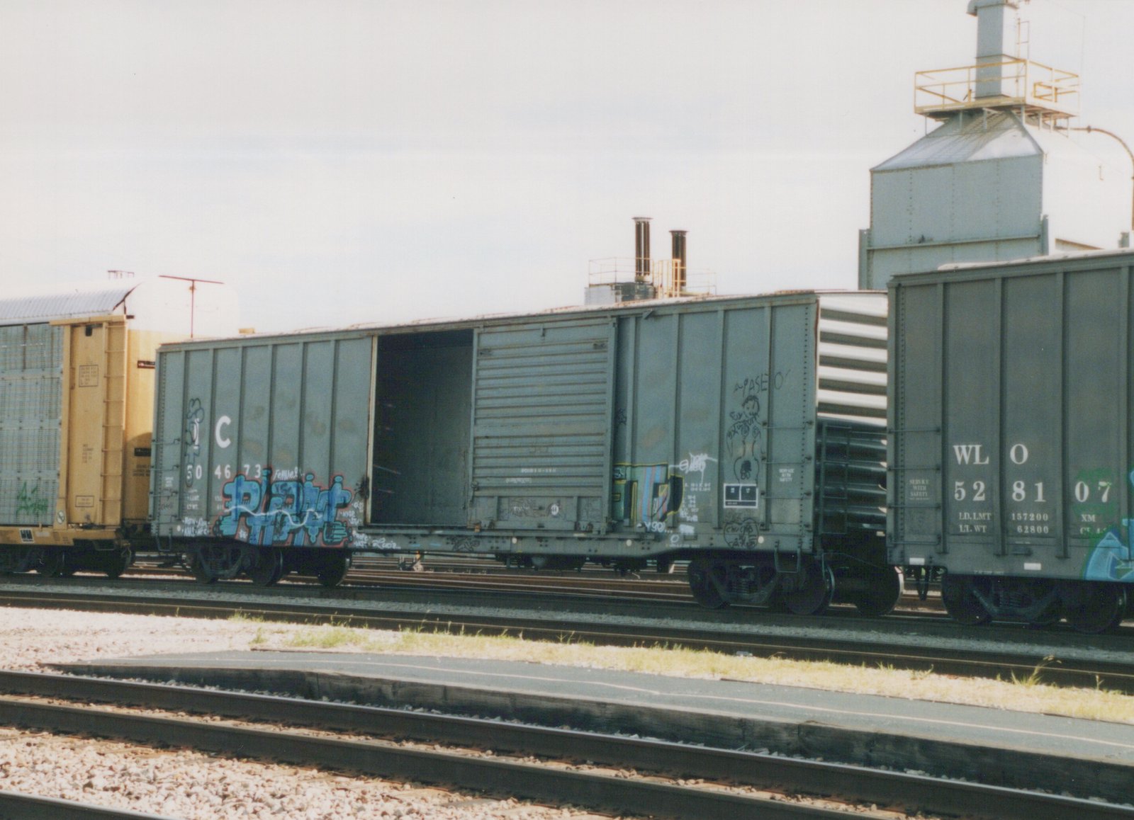 Several boxcars, including Illinois Central 504673 and WL O 528107, are parked on parallel tracks in a gravel yard, with industrial buildings in the background.
