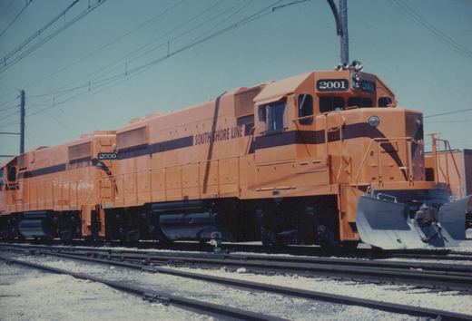 Two orange South Shore Line diesel locomotives, numbered 2001 and 2000, parked on parallel tracks in a sunny yard.