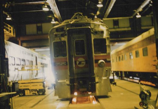 A front view of a silver and red South Shore Line train car, number 32, with an RTA logo, parked inside a well-lit train shop with other cars and equipment nearby.