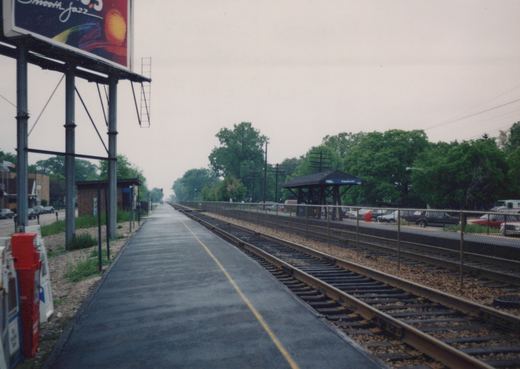 An empty train station platform with a large billboard for 'Smooth Jazz' on the left and a shelter with a blue 'Edgebrook' sign on the right, under an overcast sky.