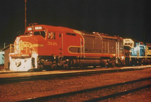 Two red and silver Santa Fe SD40 diesel locomotives, numbered 5948 and 5920, are coupled together on a railroad track at night in a yard.
