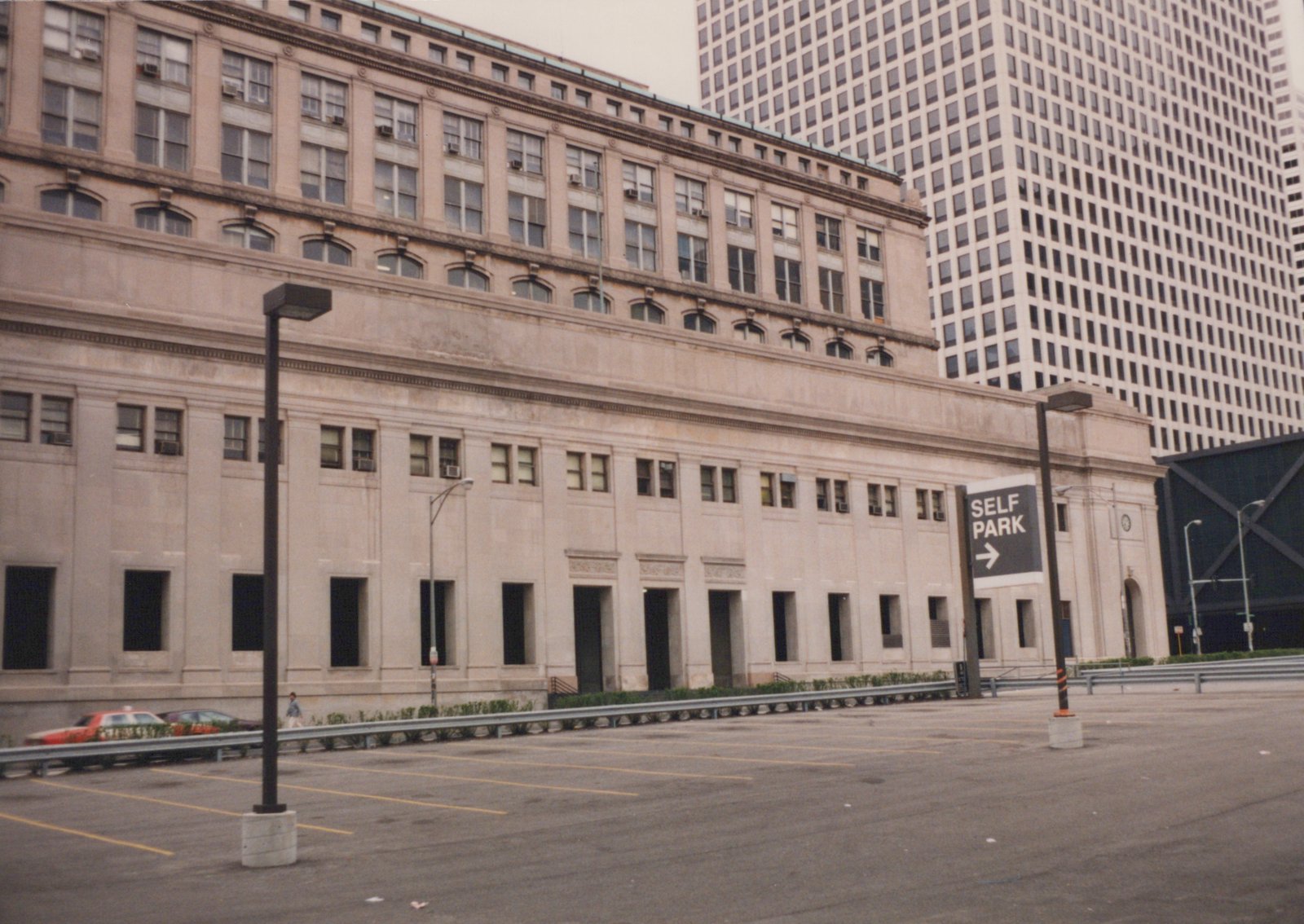 An overcast day at a large, windowed building in Chicago with a 'SELF PARK' sign and a few parked cars nearby.
