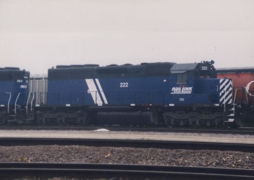 Side view of a blue IEM Rail Link diesel locomotive, number 222, on railroad tracks in a yard on an overcast day.