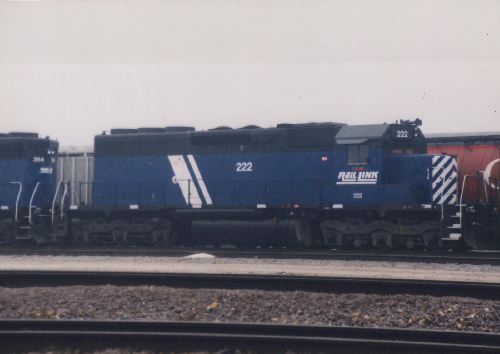 Side view of a blue IEM Rail Link diesel locomotive, number 222, on railroad tracks in a yard on an overcast day.