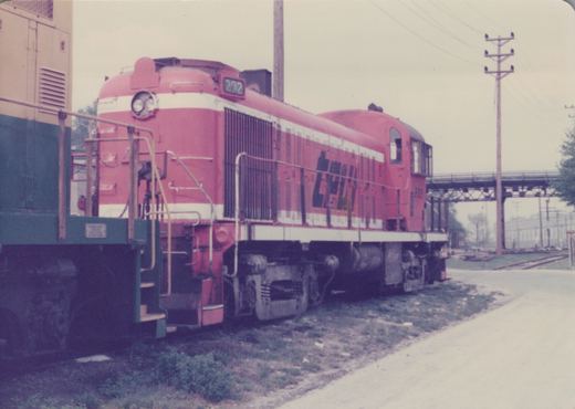 A red and white diesel locomotive with the number 202 and 'CHICAGO & NORTH WESTERN' lettering is shown in a three-quarter front view in a rail yard.