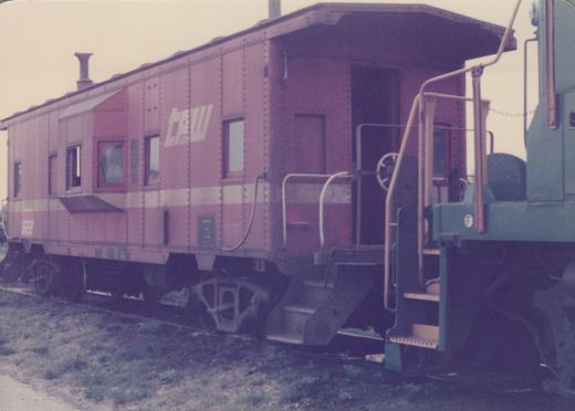 A vintage maroon and white Chicago Great Western caboose, numbered 522, photographed from a three-quarter rear angle on a grassy trackside.