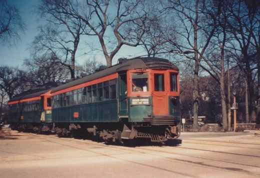 Green and orange interurban train on a street with bare trees, showing destination 'CHICAGO-EXPRESS SHORE LINE ROUTE' and number 164.
