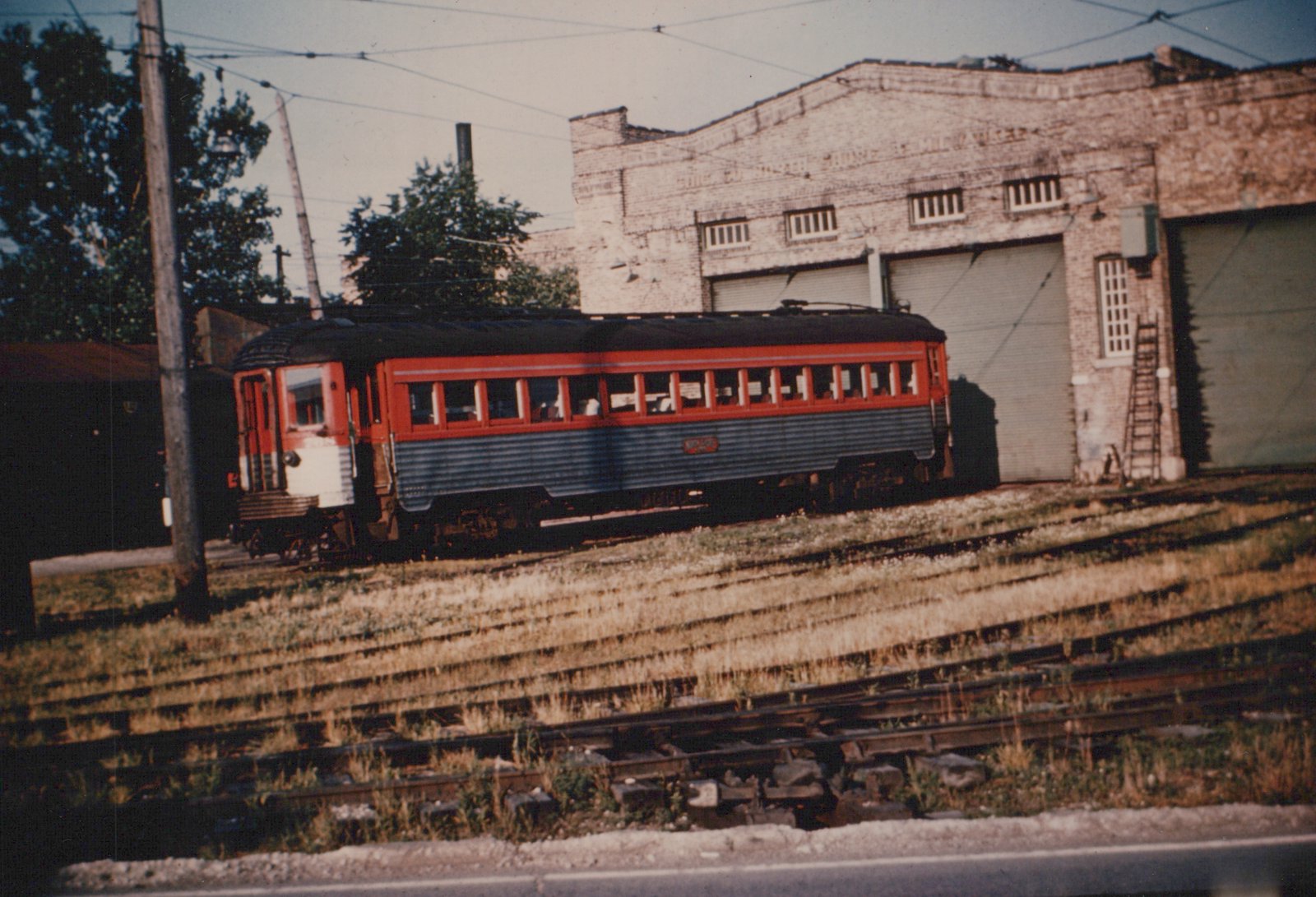 A red and grey interurban car with the number 450 is parked on tracks in front of a brick building that reads 'Chicago North Shore and Milwaukee'.