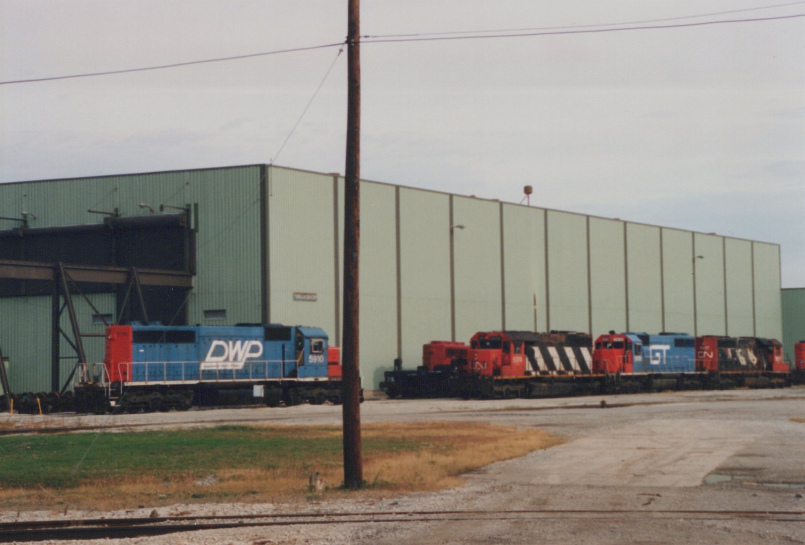 A blue and red DWP locomotive numbered 5910 is parked in a yard beside a Grand Trunk Western locomotive and Canadian National locomotives, under an overcast sky.