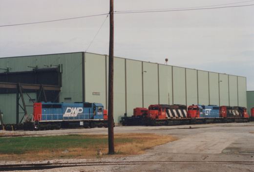 A blue and red DWP locomotive numbered 5910 is parked in a yard beside a Grand Trunk Western locomotive and Canadian National locomotives, under an overcast sky.