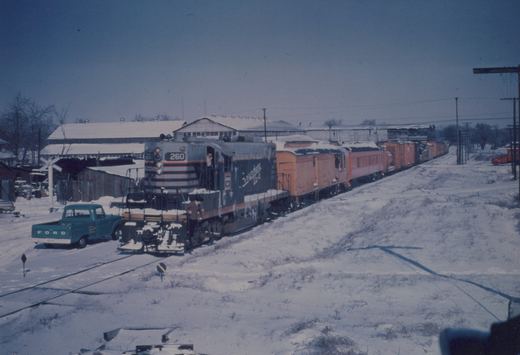 A diesel locomotive numbered 260, painted in Chicago Burlington and Quincy livery, leads a freight train through a snow-covered scene next to a blue Ford pickup truck.