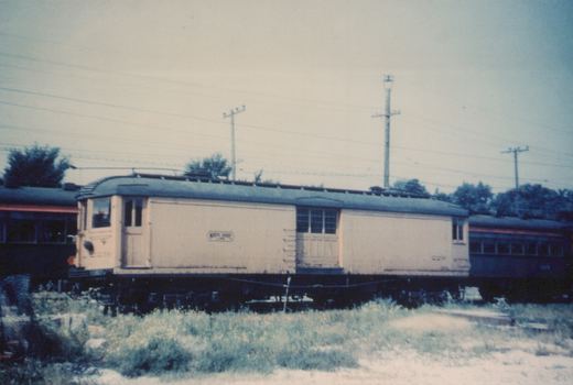 Side view of a cream-colored North Shore Line Master Unit interurban car, number 2219, on tracks surrounded by overgrown vegetation and overhead wires.