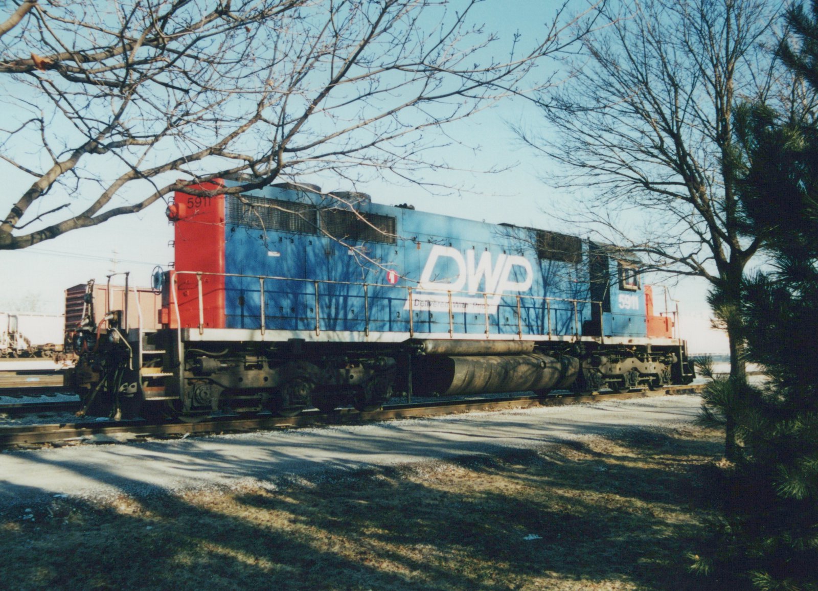 A blue and red diesel locomotive with the letters DWP and number 5911, parked on tracks surrounded by bare trees under a clear sky.