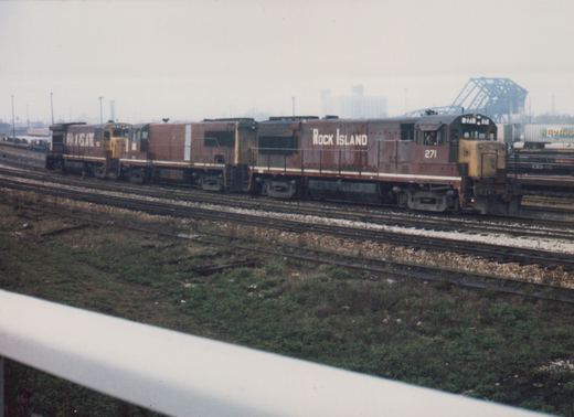 Two diesel locomotives in Rock Island livery, numbered 271 and 253, are pictured on multiple tracks in a rail yard with a hazy background.