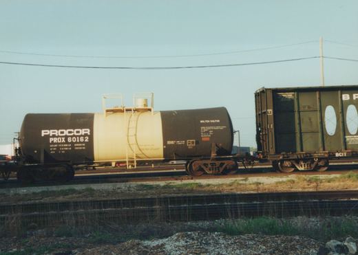 Side view of a black and cream PROCOR tank car numbered 60162 for molten sulfur on a railroad track, with a dark green BCIT boxcar visible behind it.