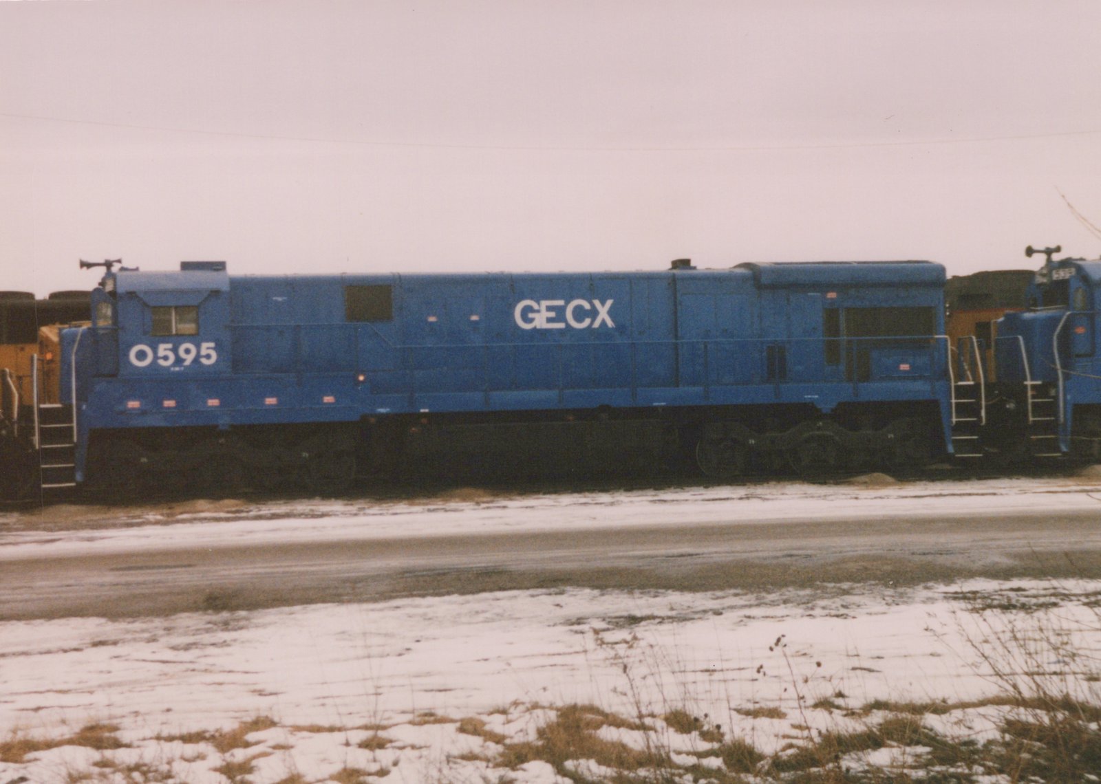 A side view of a blue GECX diesel locomotive, number 0595, parked in a snowy rail yard.