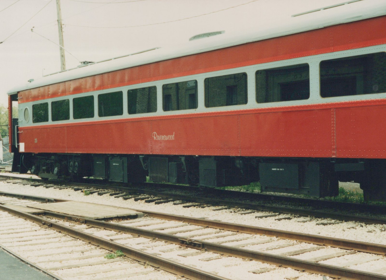 A red and white interurban railcar with the number 25 and the name Ravenswood on its side, sitting on tracks in a yard.