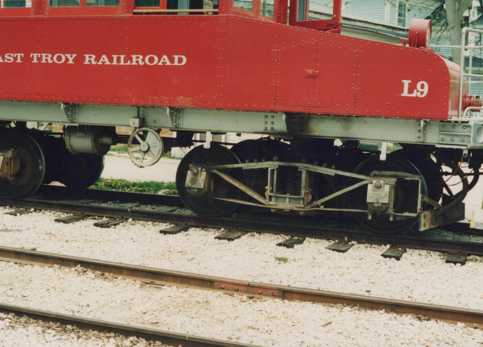 Side view of a red self-propelled railcar with 'EAST TROY RAILROAD' and 'L9' lettering on a gravel-ballasted track.