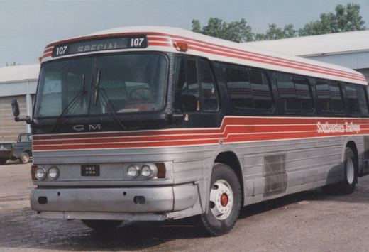 A silver and red Southeastern Trailways motor bus, number 107, is parked on a gravel lot with a green pickup truck in the background.