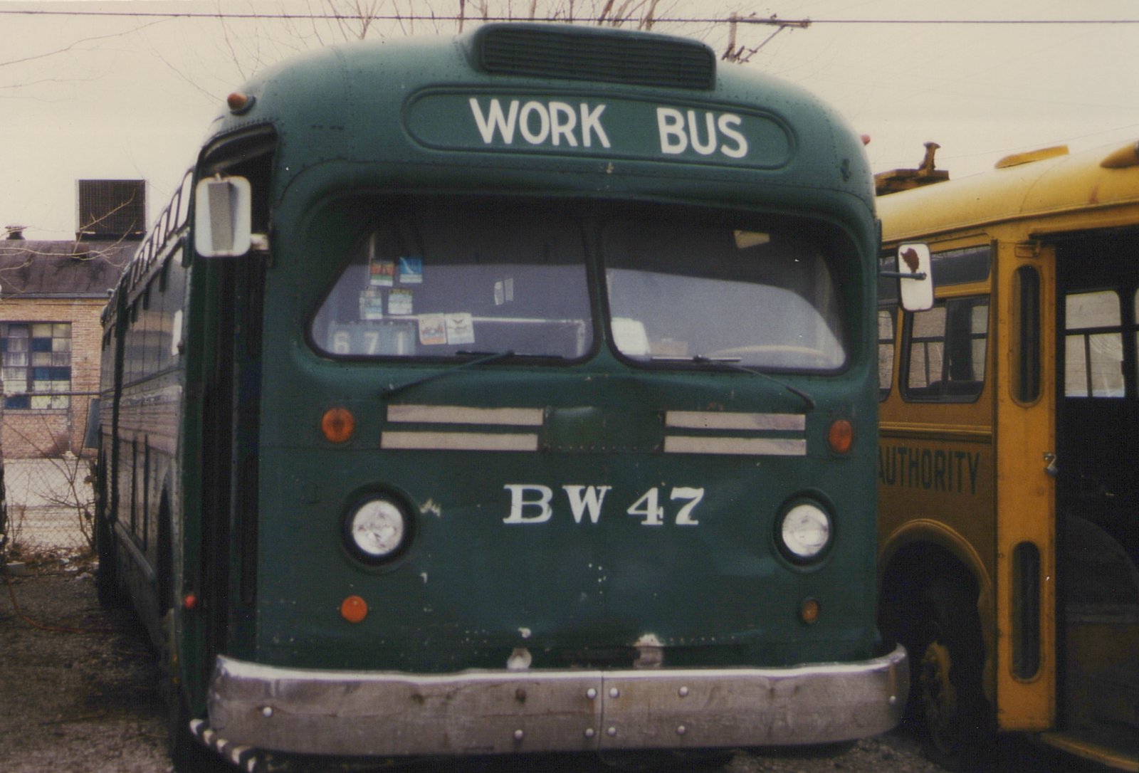 Front view of a dark green CTA work bus labeled 'BW 47' parked next to a yellow bus in a yard.