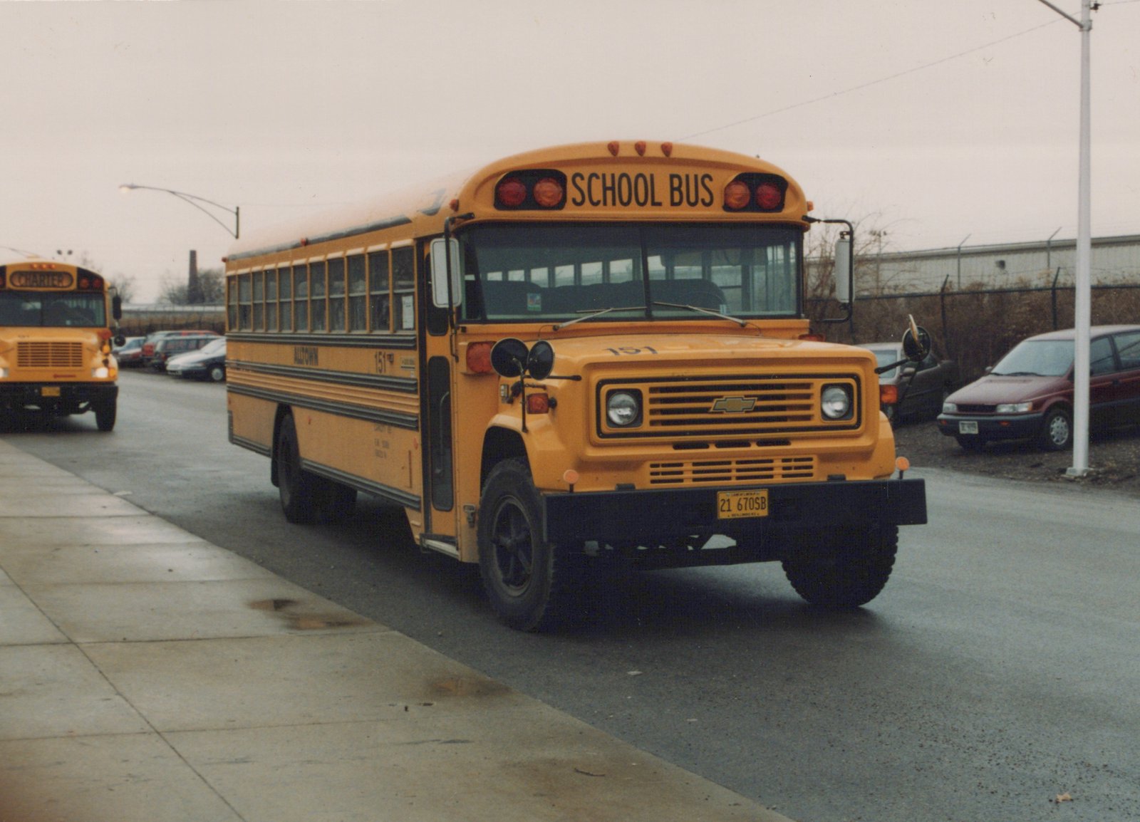 A yellow Alltown school bus numbered 151, with a 'SCHOOL BUS' sign on top, is driving down a wet street; another school bus with a 'CHARTER' sign is visible in the background.