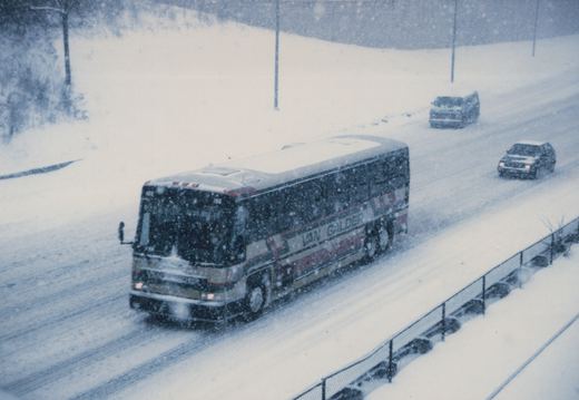 A Van Galder bus, number 118, drives on a snowy road with cars behind it, amidst falling snow.