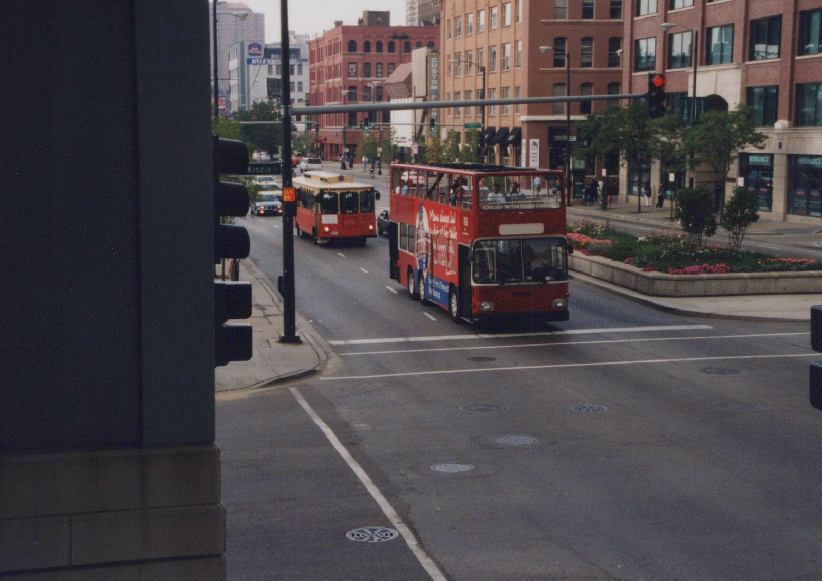 A red double-decker bus with 'Chicago Motor Coach Company' lettering and the number 568 is turning at an intersection with a single-decker bus behind it, in a city street scene with buildings and pedestrians.